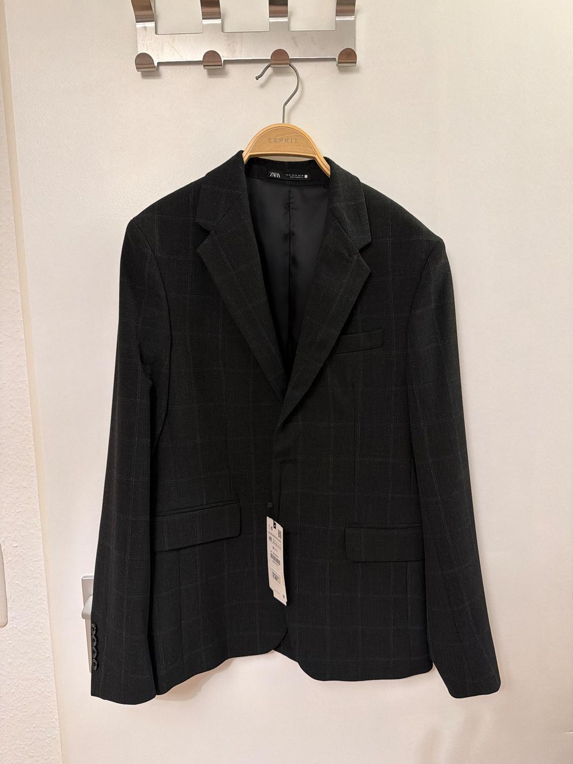 Black checked jacket hanging on a wooden hanger with a visible label. White background and metal clothes rail.