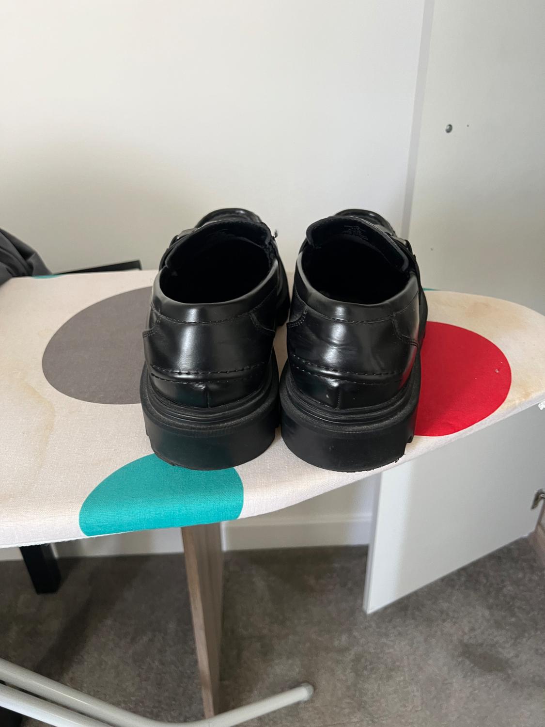 Pair of black loafers seen from behind, resting on an ironing board with a colourful polka dot cover.