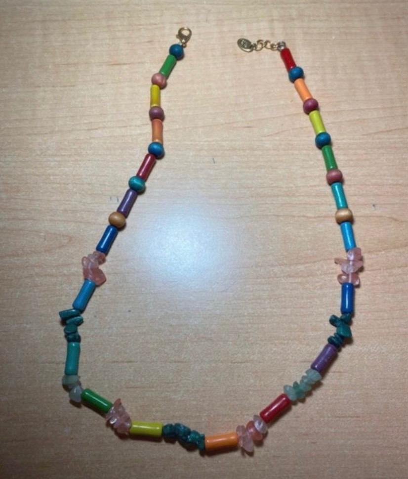 Casual colourful beaded necklace with cylindrical shapes and irregular stones, displayed on a light wood surface.