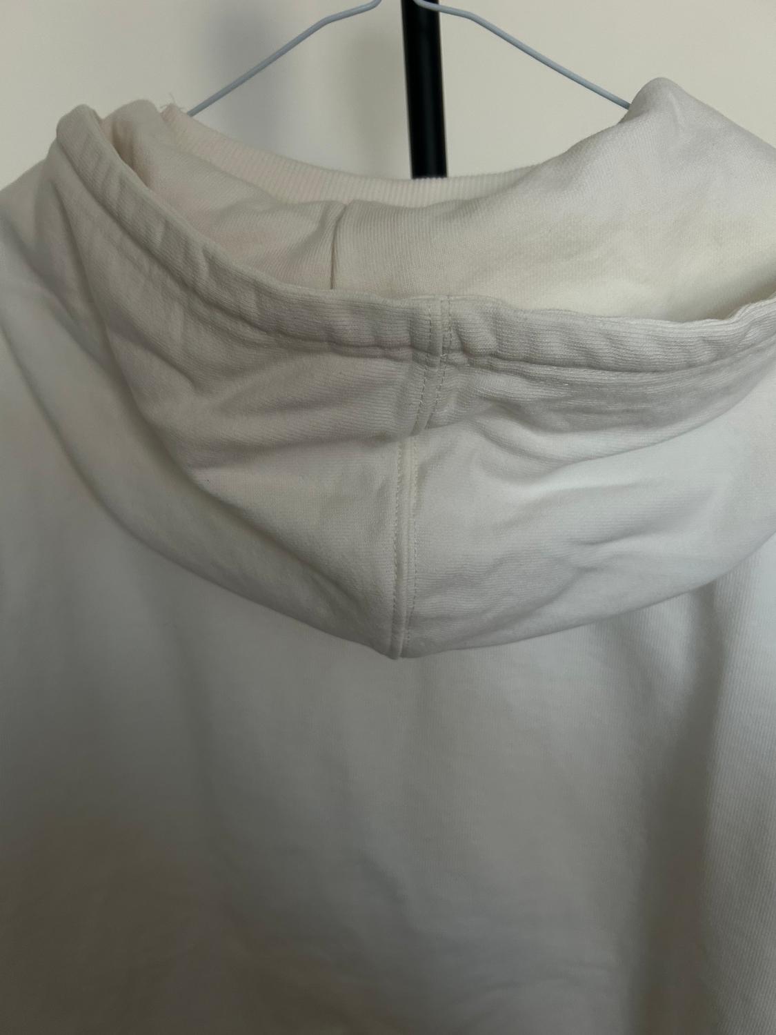 White hooded sweatshirt hanging on a hanger. The fabric looks soft and comfortable, with visible seams on the back.
