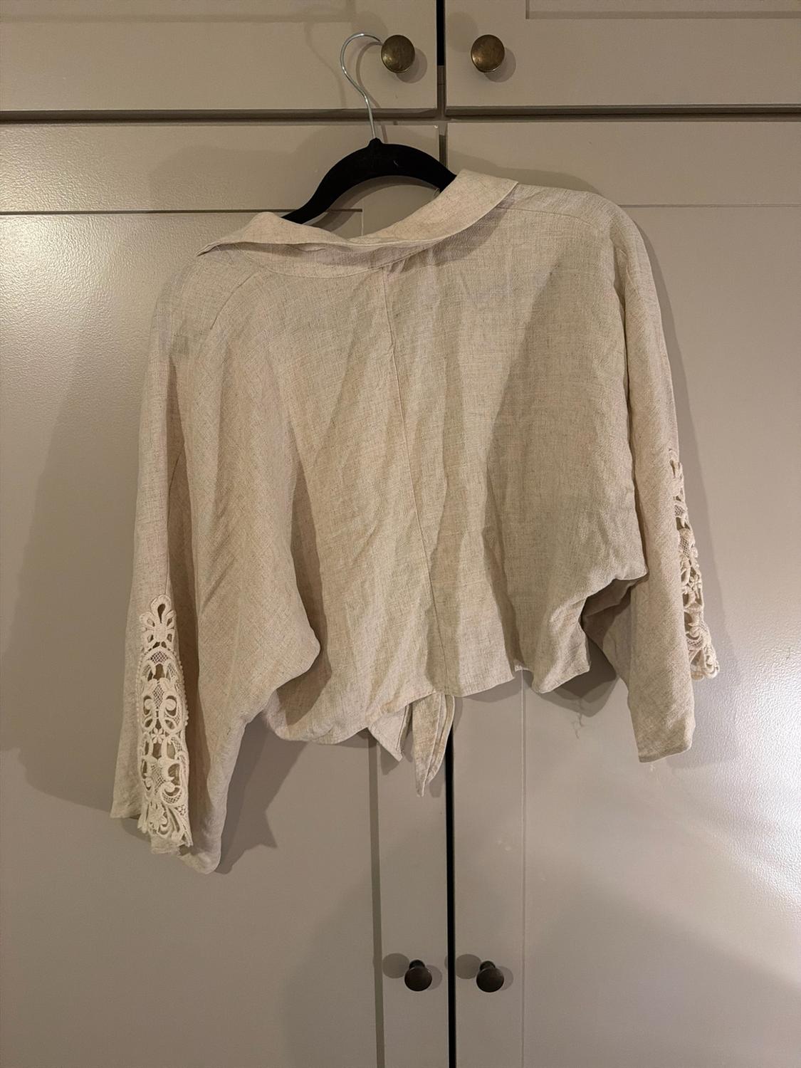 Beige blouse with a collar and lace details on the sleeves, hanging on a black hanger in front of wardrobe doors.