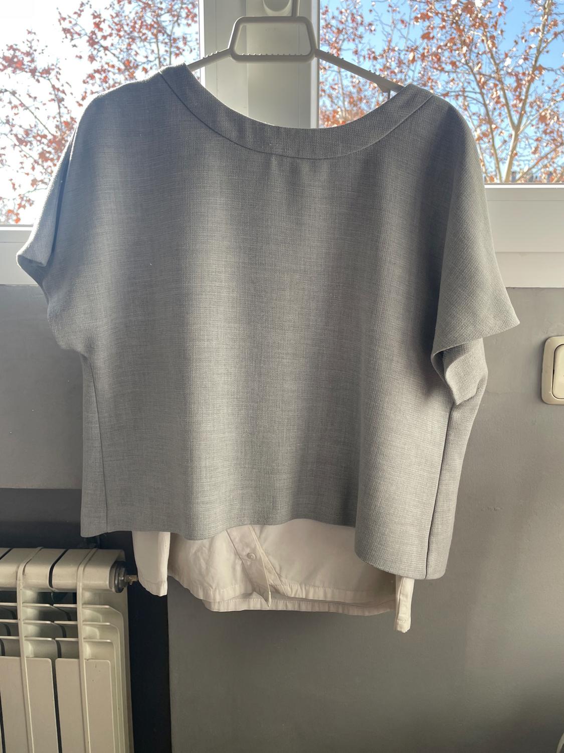 Rear view of a grey crew neck, short-sleeved blouse over a white shirt peeking out underneath.