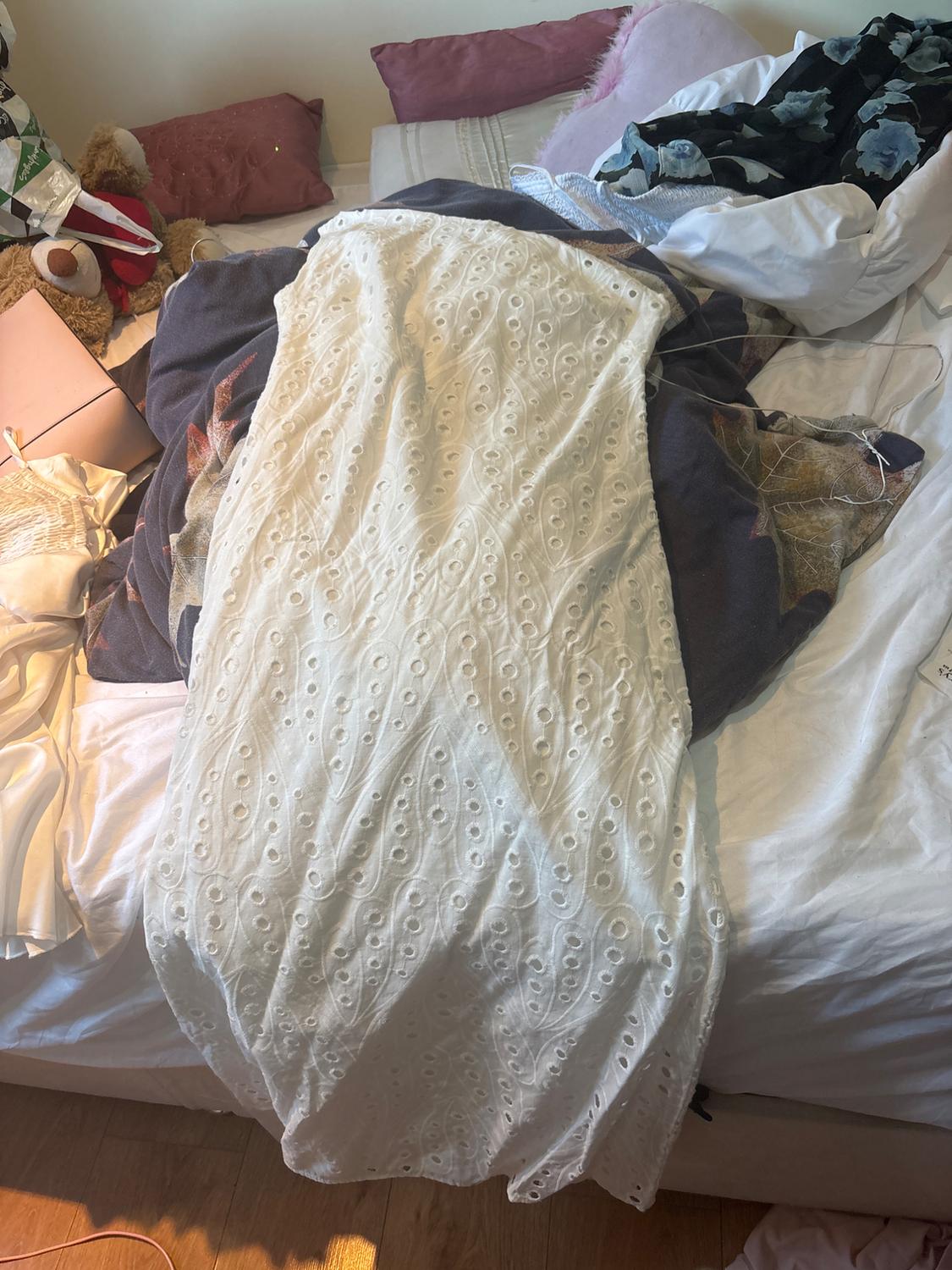 White dress with openwork detailing laid out on a messy bed with sheets, pillows and other garments in a relaxed setting.