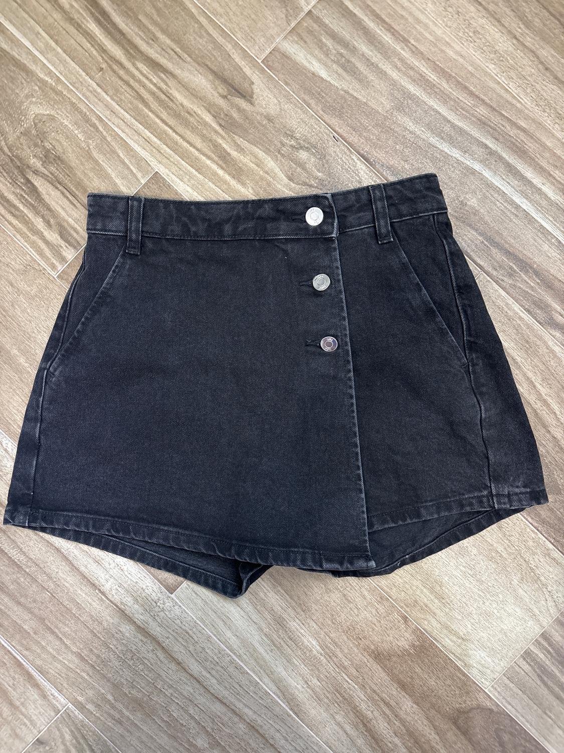 Black mini skirt with front buttons on a light wooden floor. Simple and modern design, ideal for a casual look.