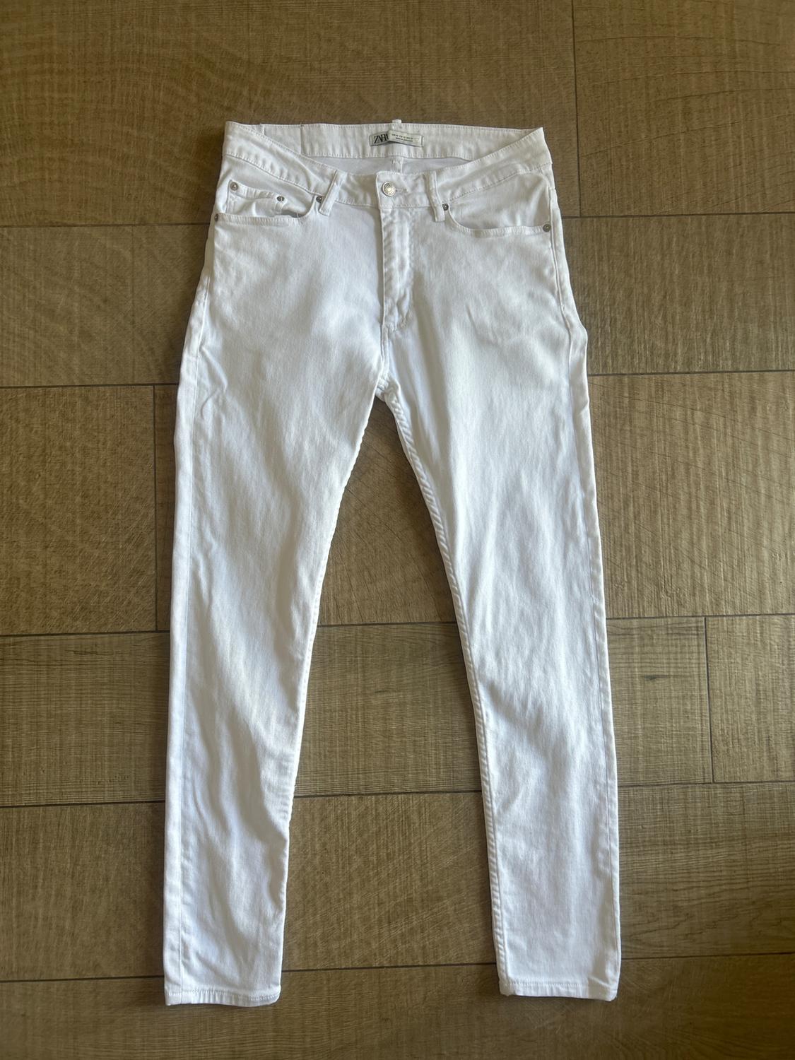 White skinny jeans with pockets and belt loops, laid out on a wooden floor.