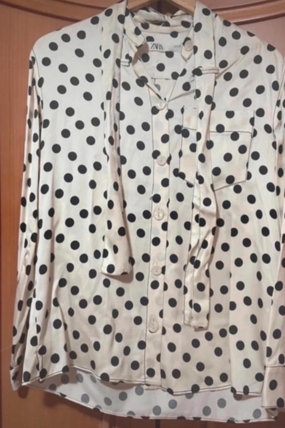 Front view of a white blouse with black polka dots and a chest pocket.