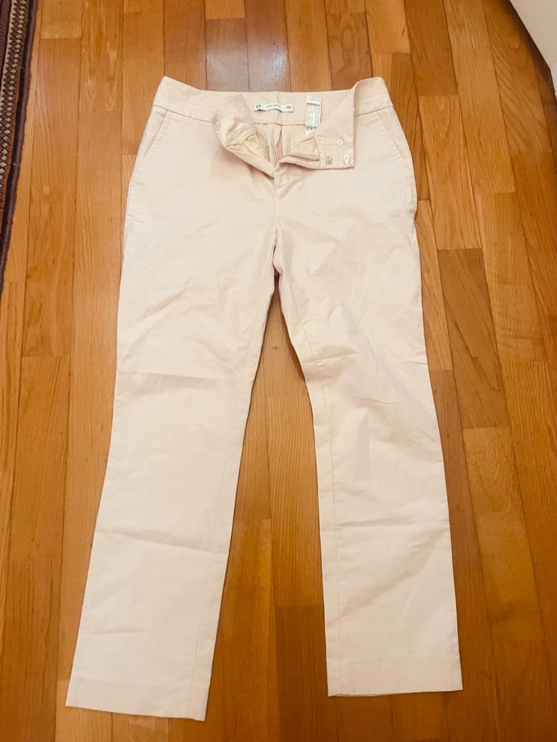 Light beige casual trousers, unbuttoned and laid out on a wooden floor. Relaxed style composition.