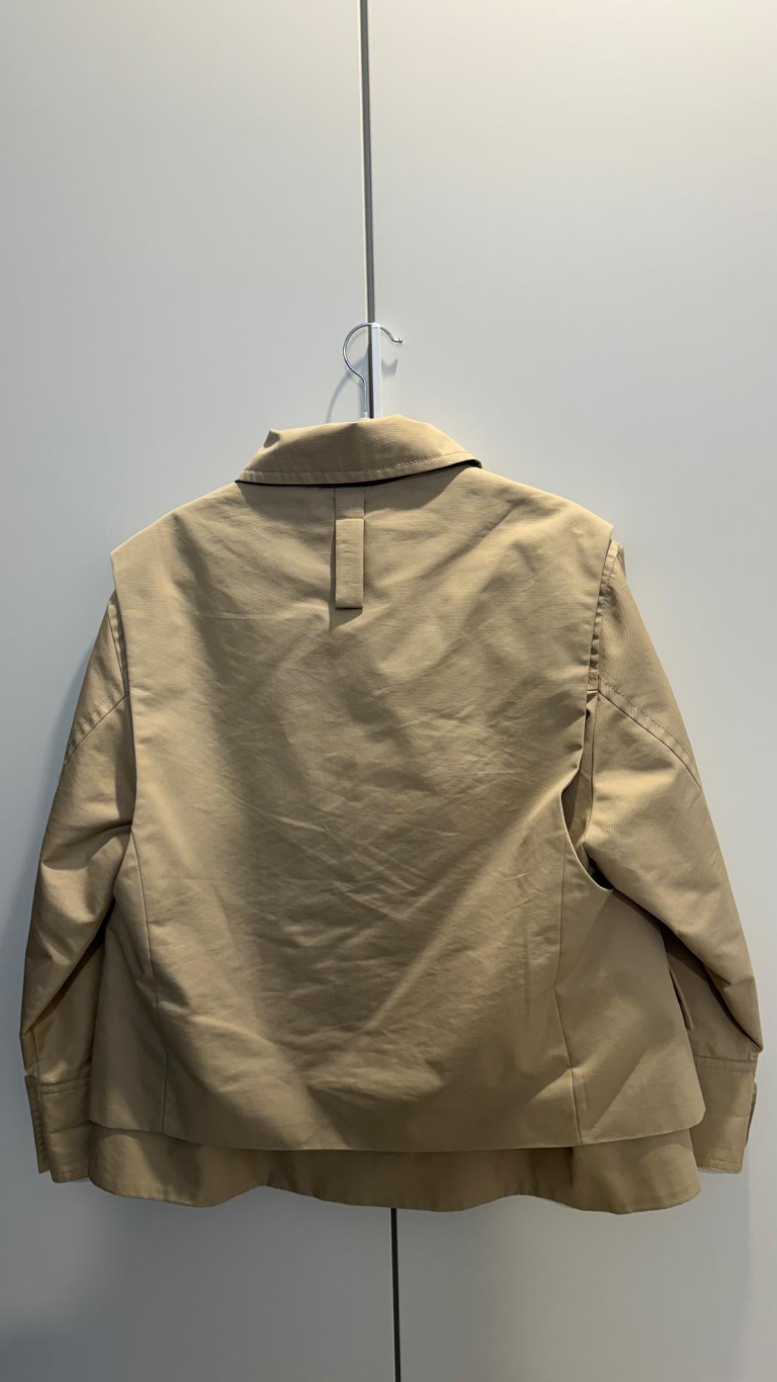 Beige jacket hanging on a hanger, rear view, against a white background.