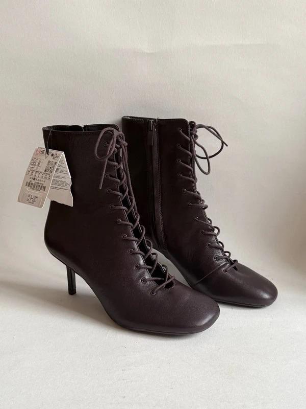 Dark-coloured high-heeled ankle boots with laces and a side zip, on a white background. Tags hanging from one of the boots.