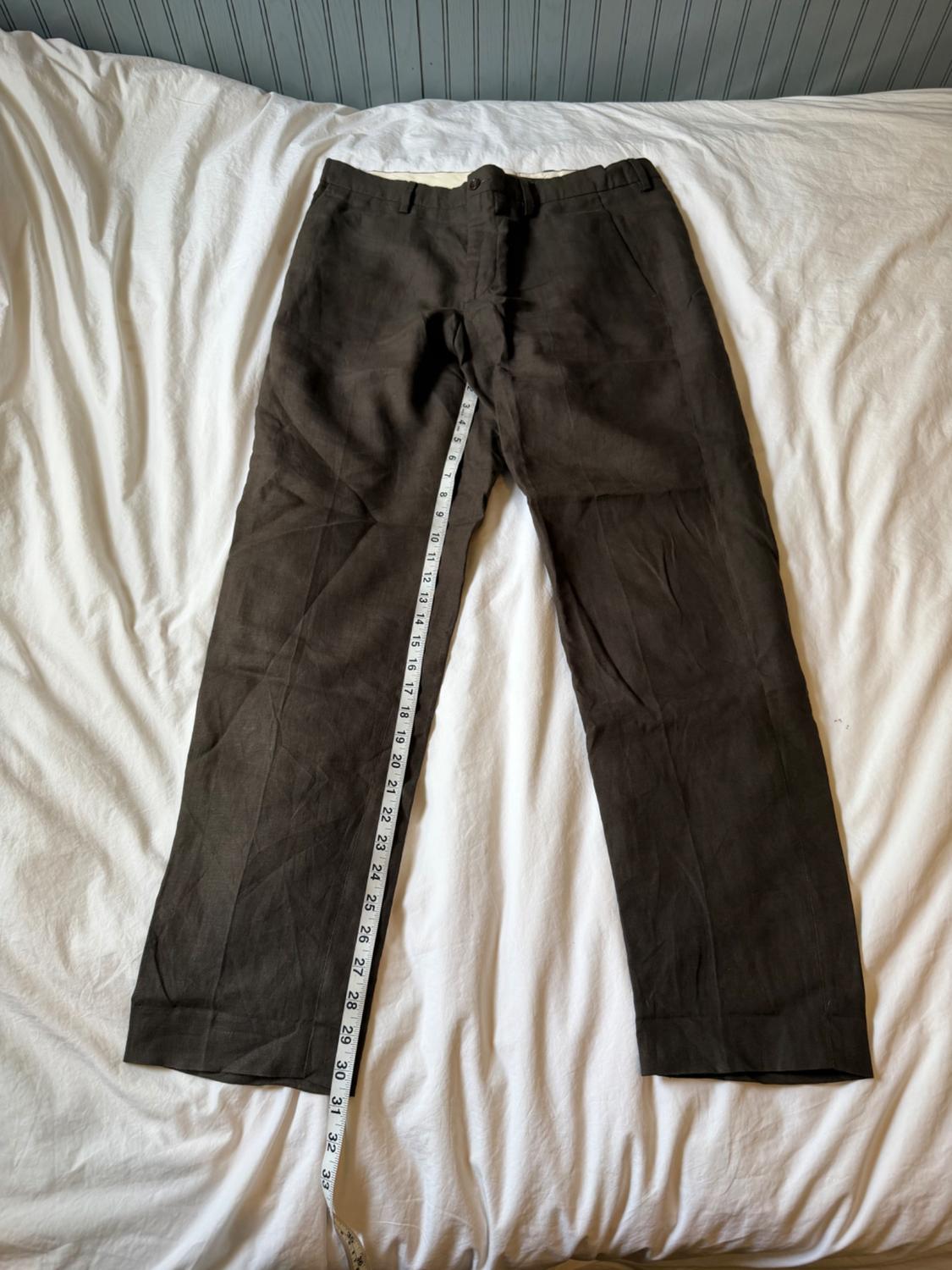 Dark brown pants laid out on a white sheet. A measuring tape measures the length of the left leg.