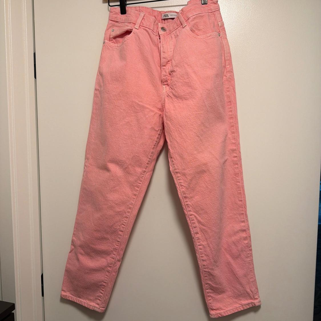 Pink casual-style jeans hanging on a black hanger in front of a white door. Label with the text ZARA.