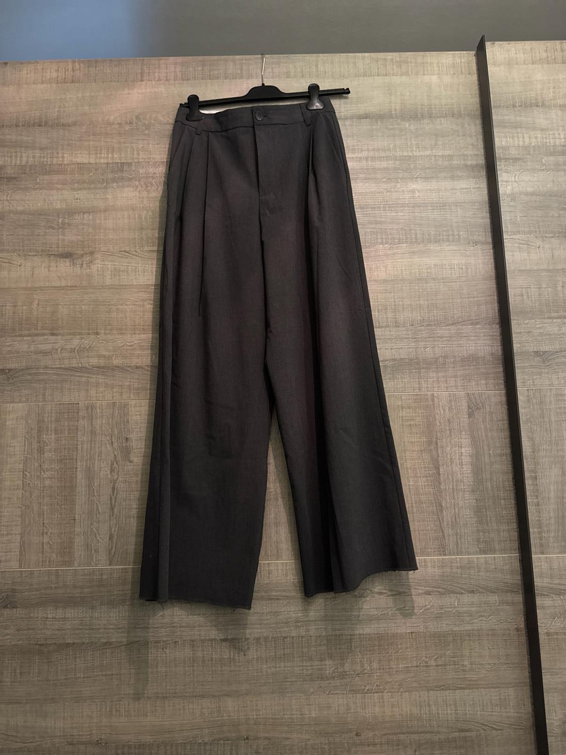 Dark grey wide-leg tailored trousers hanging on a black hanger in front of a wooden wardrobe. Casual style with a relaxed vibe.