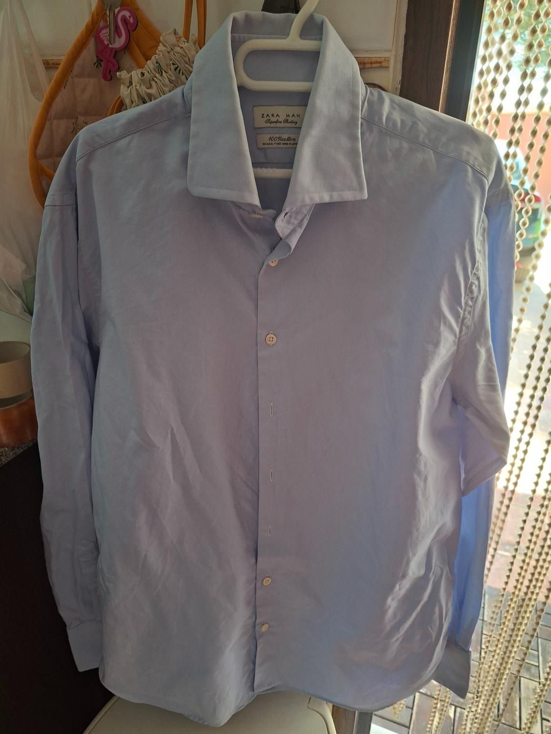 Light blue shirt on a hanger in a relaxed setting. Text: ZARA MAN Superfine Shirting 100% cotton.