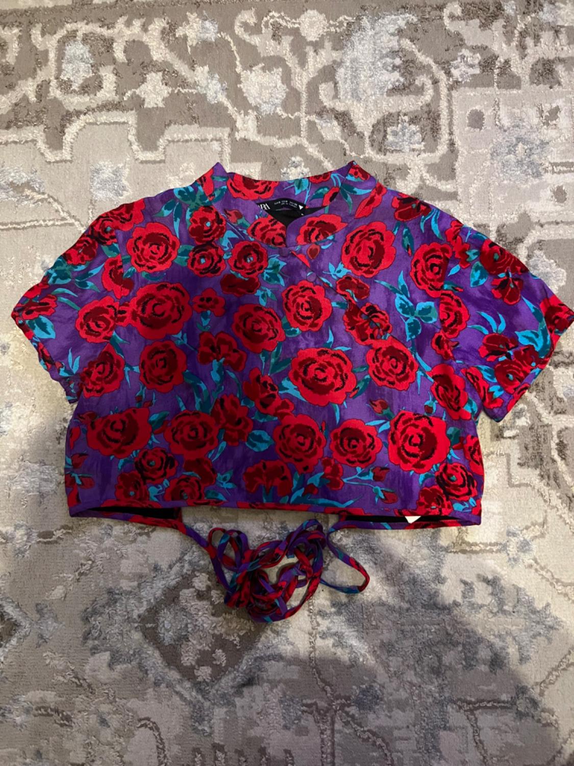 Short-sleeved crop top with a red rose and green leaf print on a purple background, over a geometric design rug.