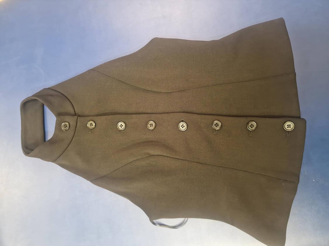 Olive green sleeveless top with a high neck and front button fastening, laid flat on a plain blue background. Fitted design with seams.