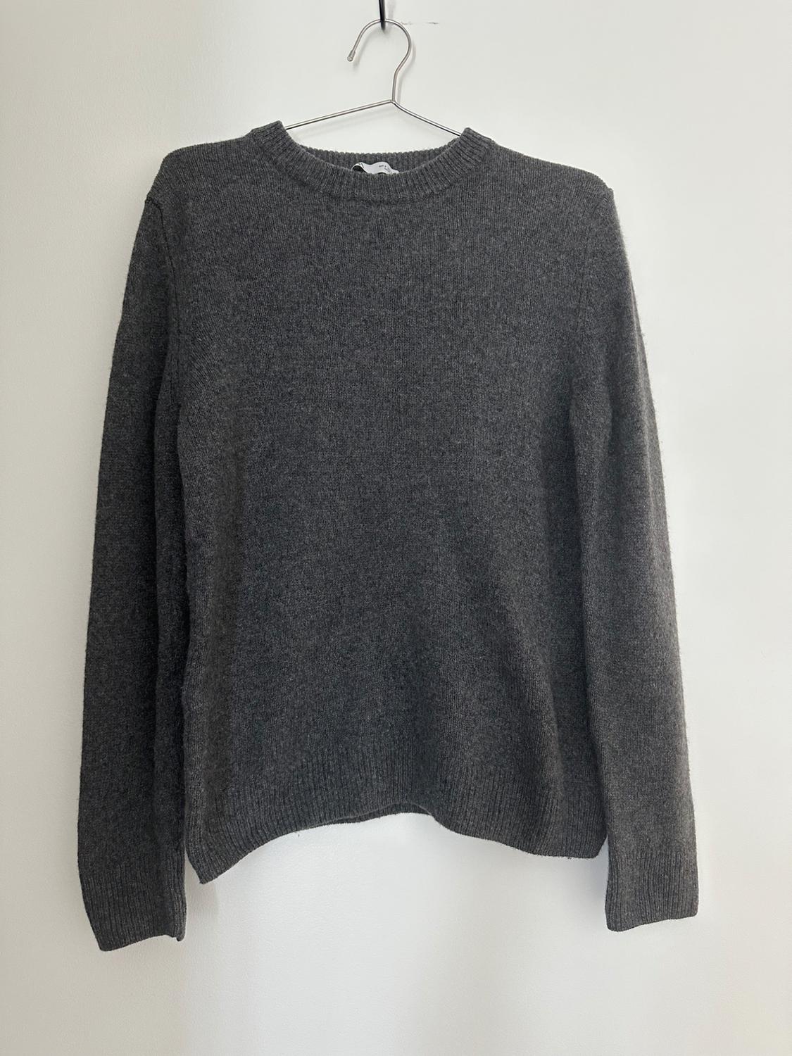 Dark gray knit sweater with a crew neck and long sleeves, hanging on a metal hanger against a white wall.