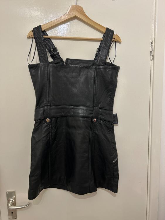 Black dress with wide straps, featuring zip and button details, hanging on a wooden hanger over a white door.