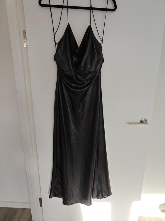 Black spaghetti-strap dress hanging on a hanger over a white door, with natural light illuminating from the right.