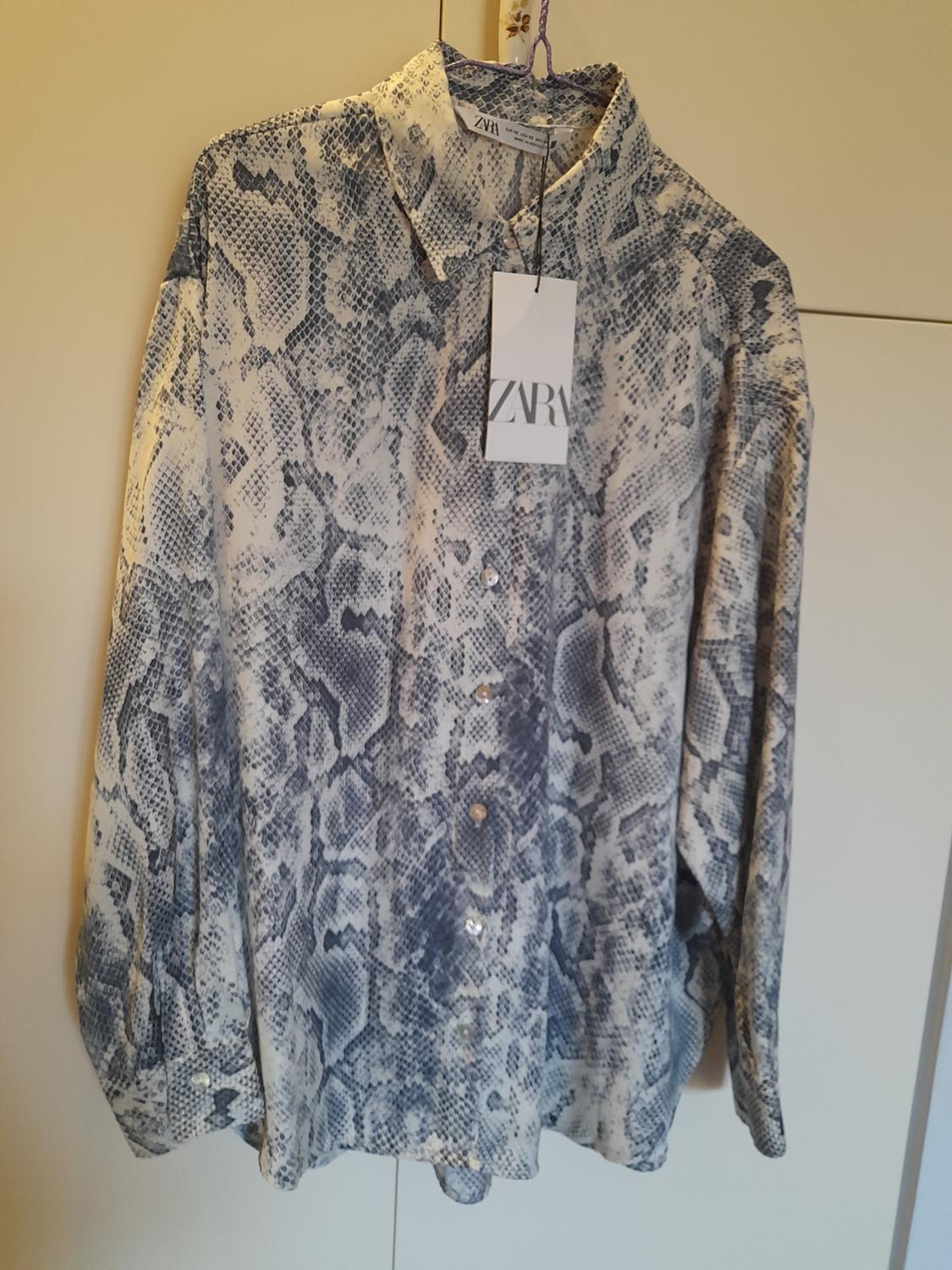 Grey snake-print long-sleeved shirt, hanging on a hanger against a light background. Label with the text ZARA.