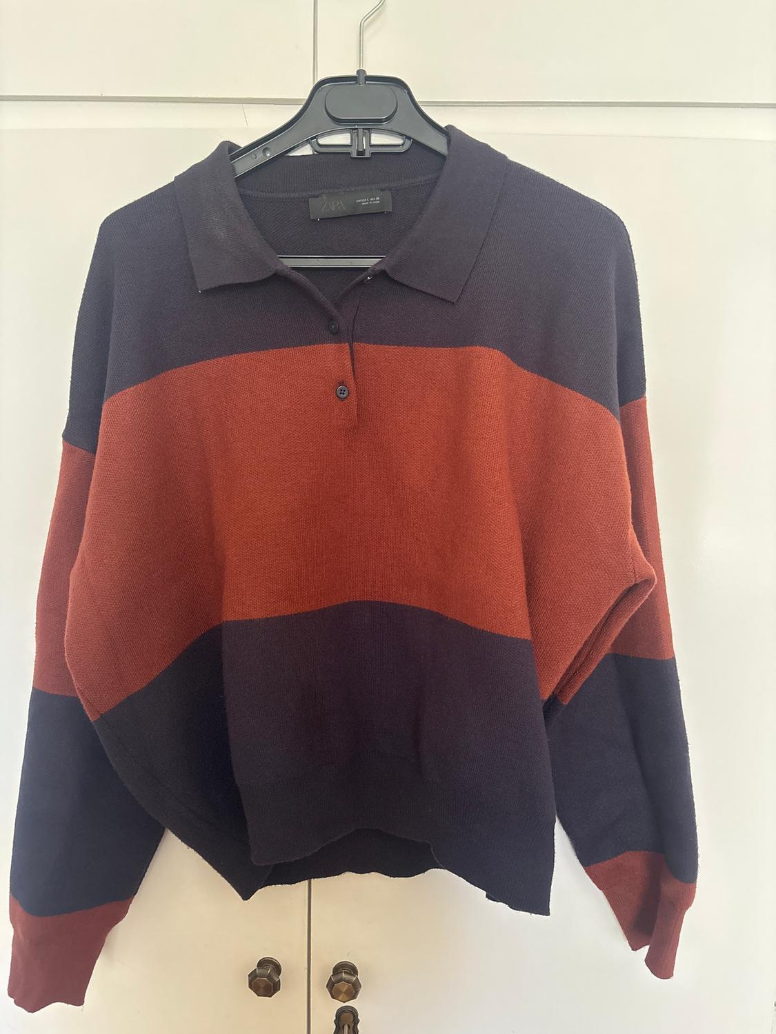Wide-striped jumper in black and red, with a polo neck and buttons, hanging on a black hanger against a white background.