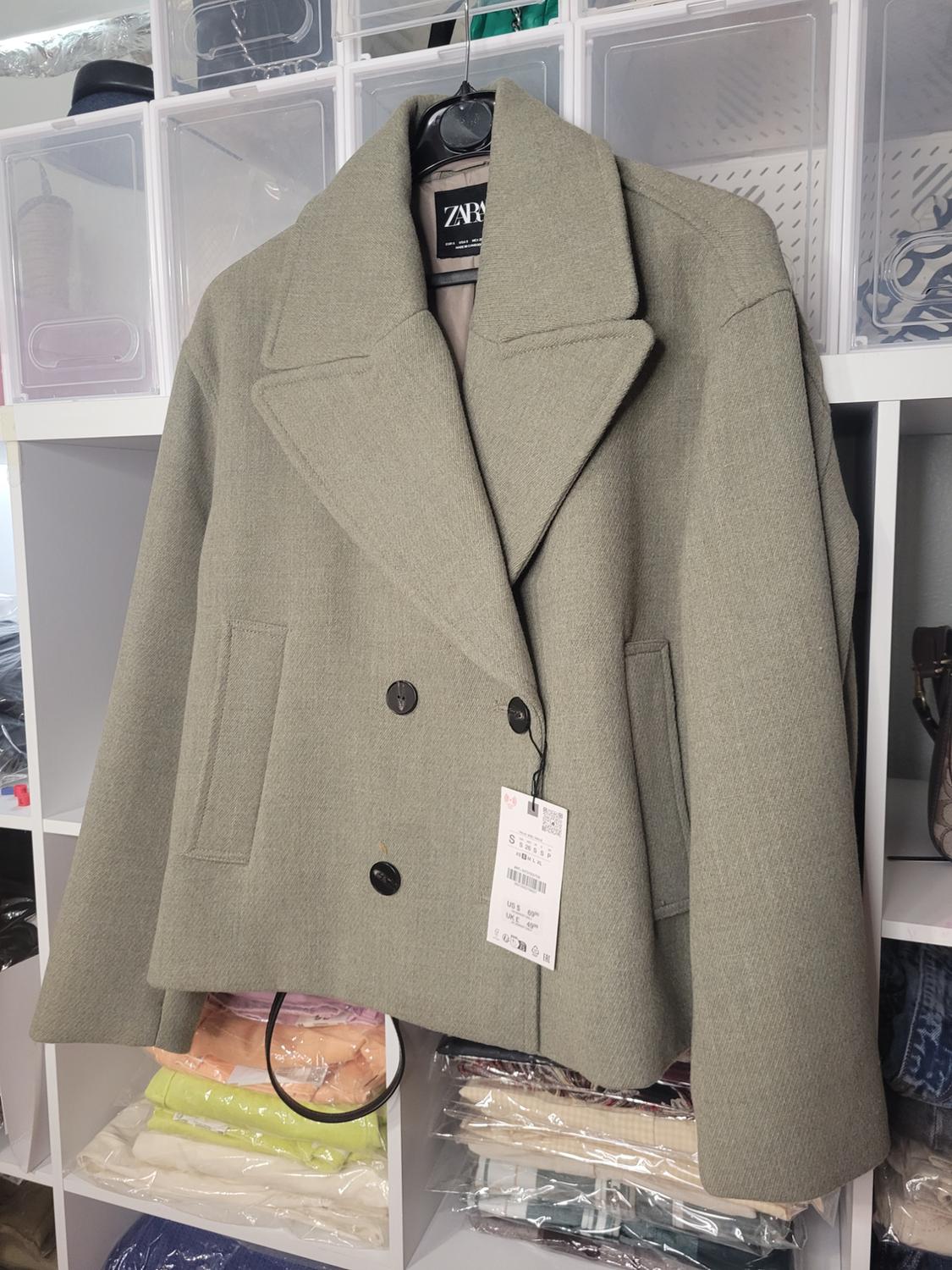 Front view of a gray jacket with wide lapels and black buttons, side pockets, hanging on a hanger.