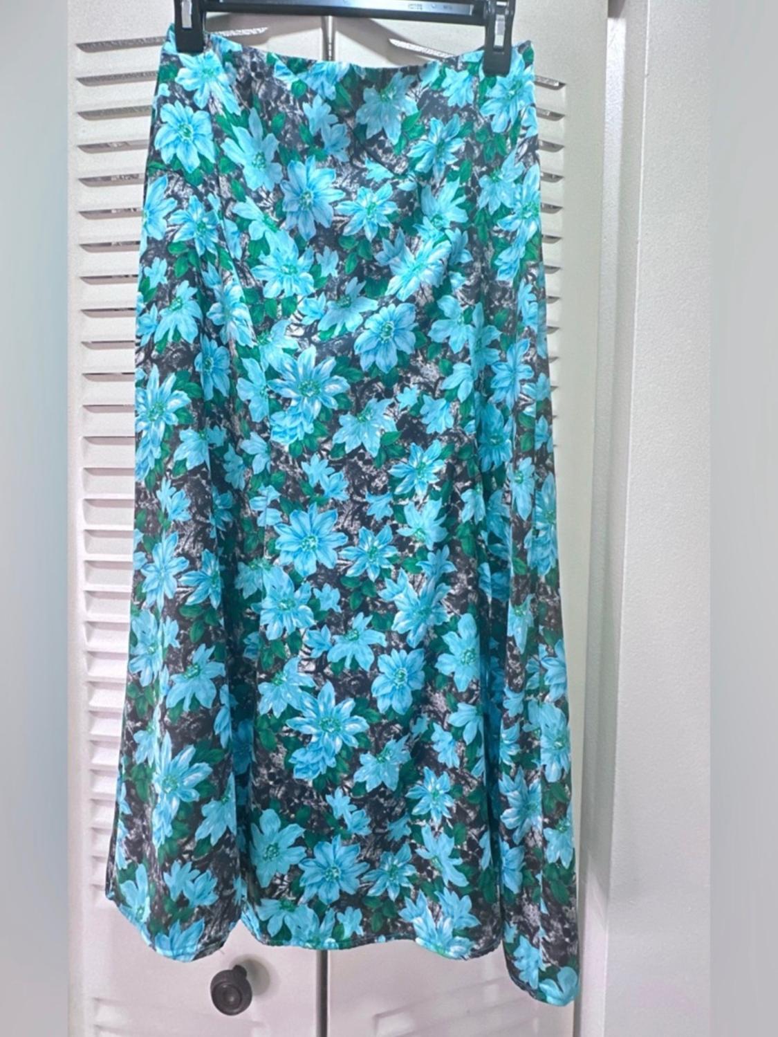 Blue and green floral print hung skirt against a black background, in an indoor setting with white louvred doors.
