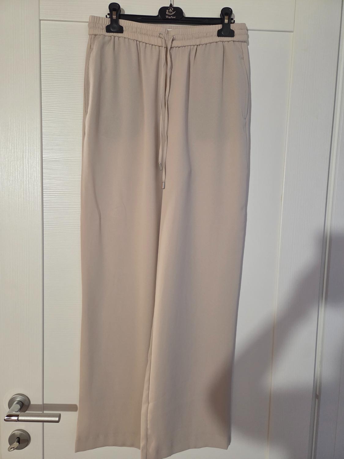 Beige trousers hanging on a black hanger over a white door. Elasticated waist with adjustable drawstring.