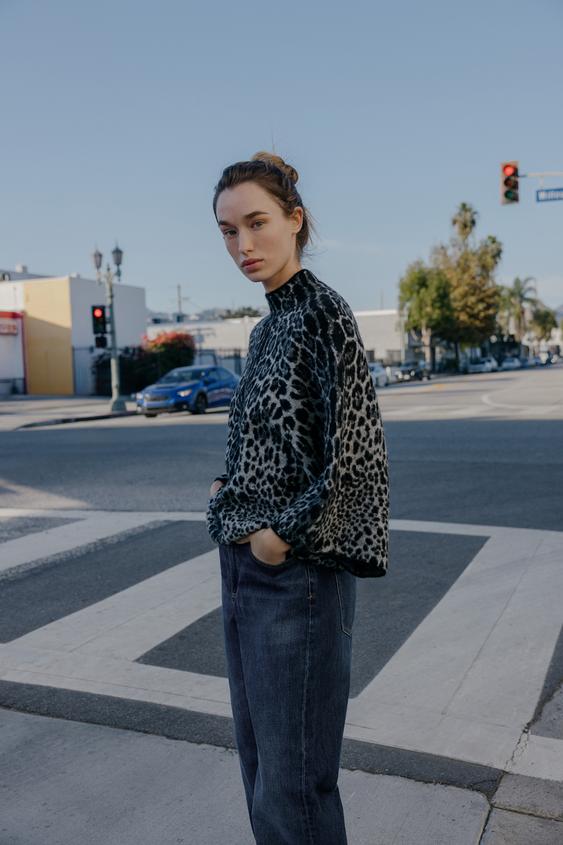 Sada svetru s potiskem animal print v černé a šedé barvě s tmavě modrými džíny a bočními kapsami.