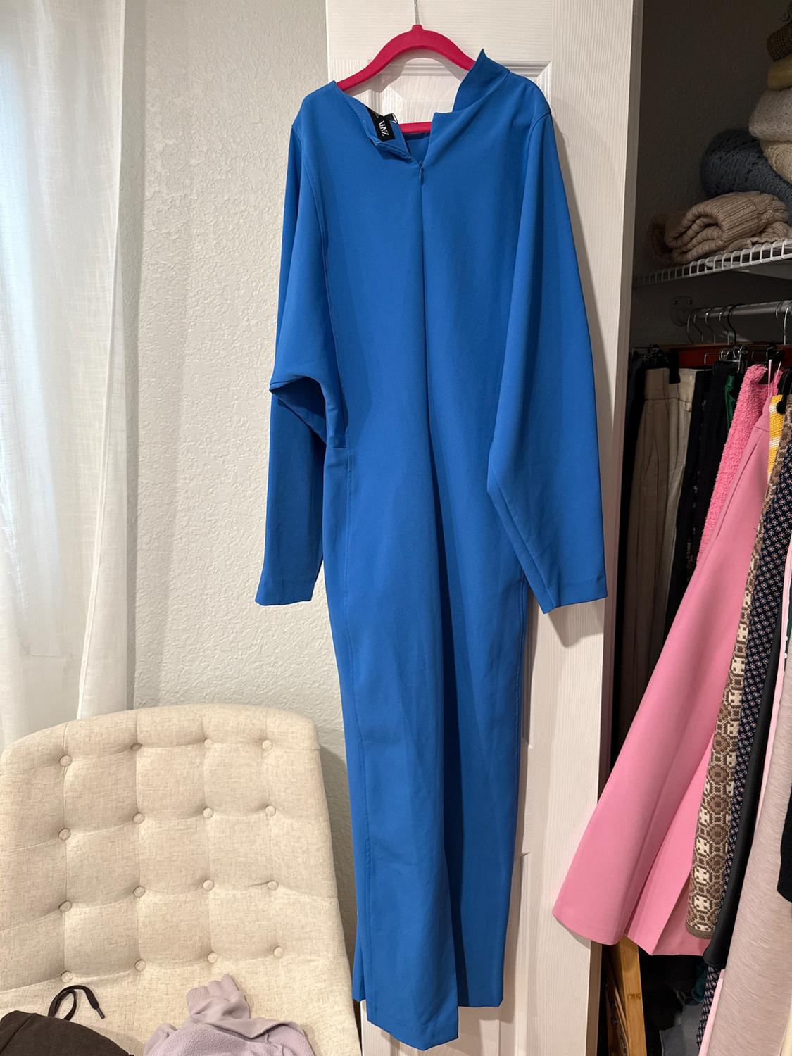 Blue monkey hung on a pink hanger over a white door. In the background, a closet with clothes and a beige chair with garments.