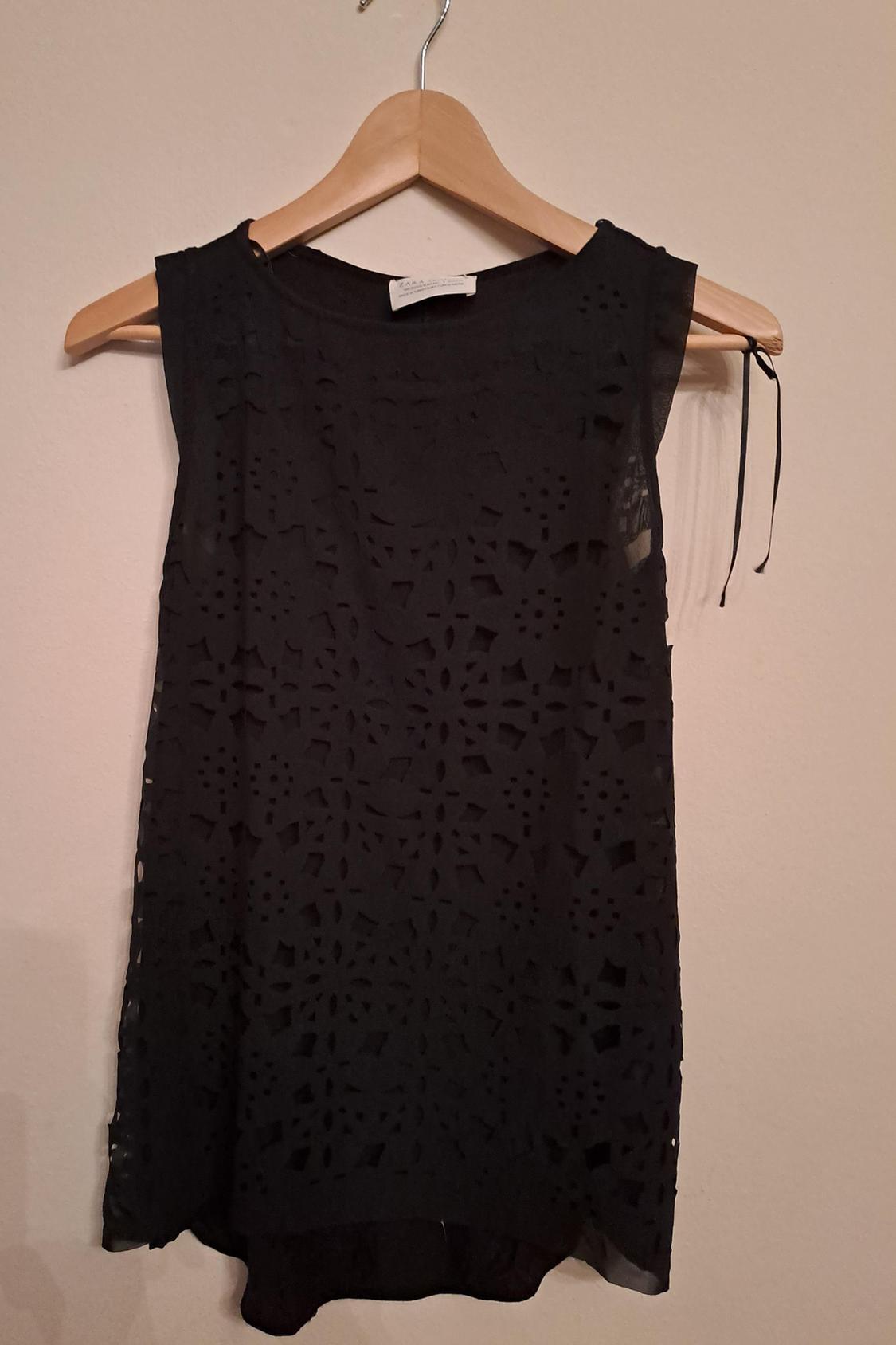 Front view of a black sleeveless crochet blouse with a tie detail on the shoulder.