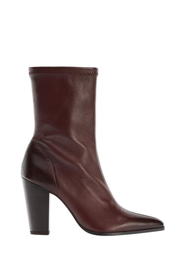 Side view of a brown boot with a high heel and pointed toe. Decorative stitching on the top of the shaft.