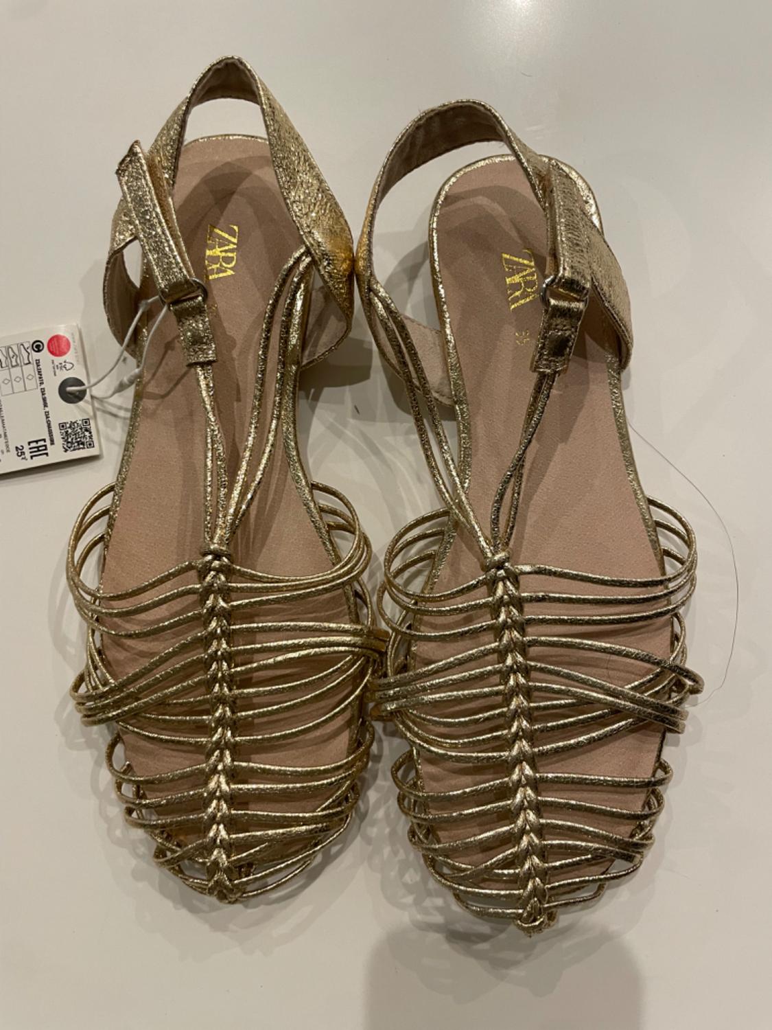 Front view of gold sandals with criss-cross straps and buckle.