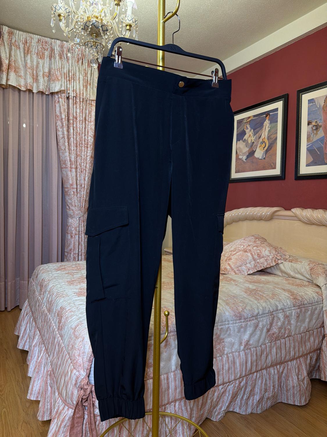 Black trousers hanging on a gold hanger in a bedroom with patterned curtains and bedspread, red walls, and decorative pictures.