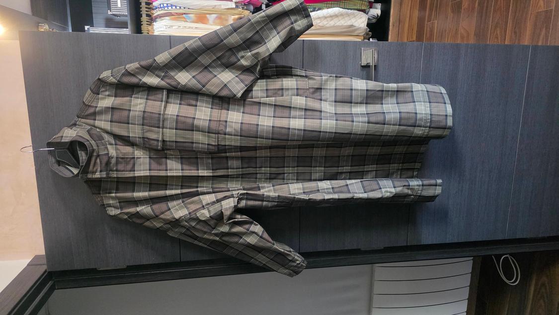 Brown and grey checked coat hanging on a dark wardrobe door, with a background of shelves and a wooden floor.