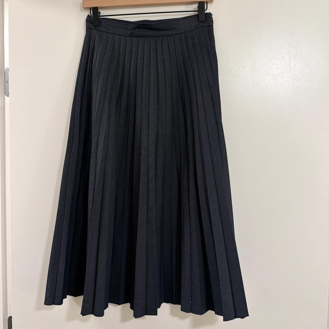 Dark grey pleated skirt hanging on a wooden hanger on a white door.