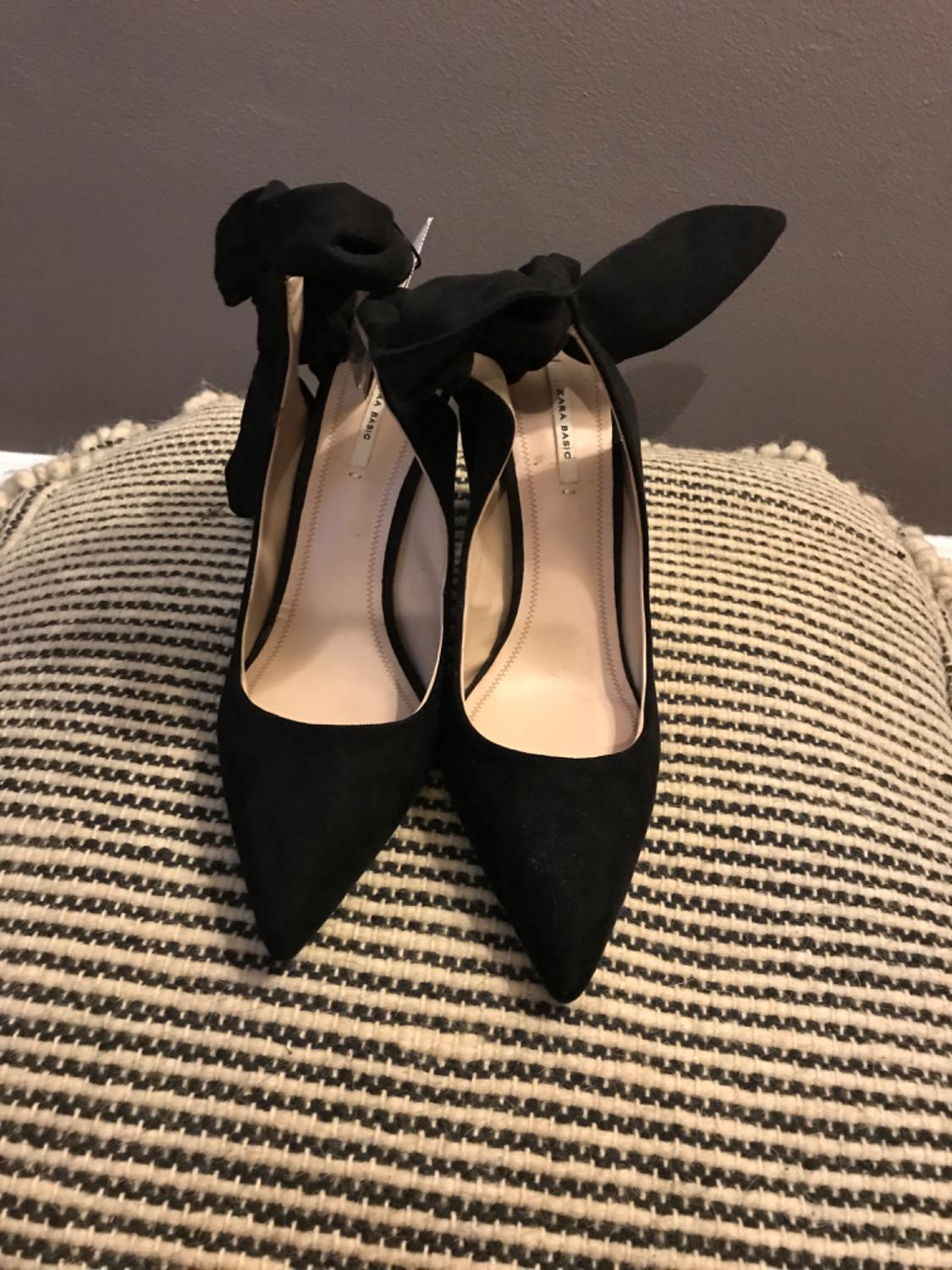 Front view of black heeled shoes with a bow.