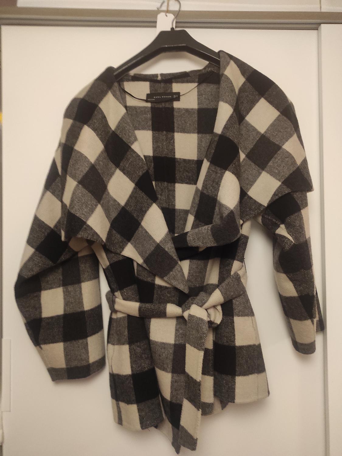 Front view of a black and white checked coat with a belt and wide lapels.