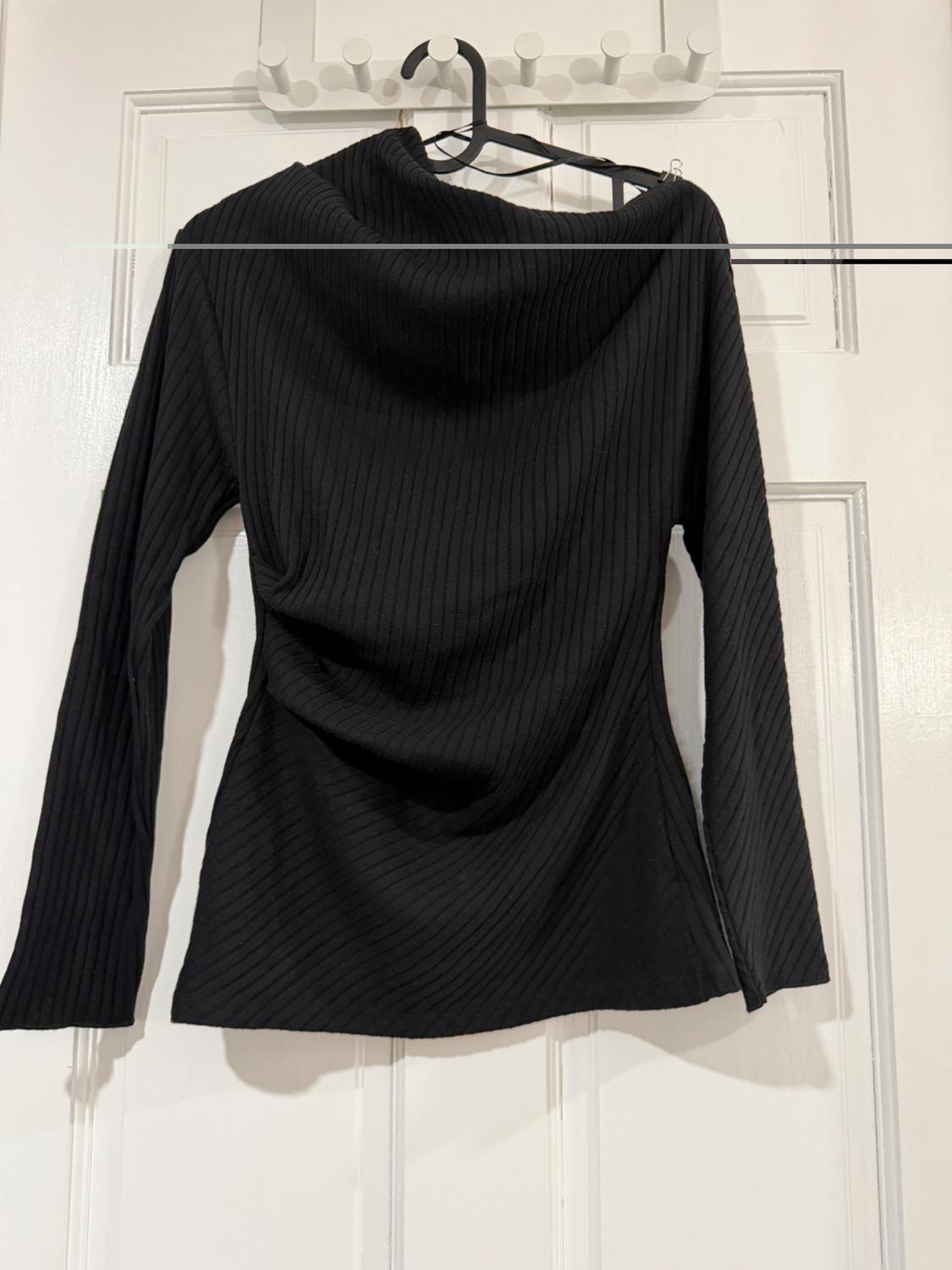 Black long-sleeved ribbed texture jumper, hung on a hanger over a white door.