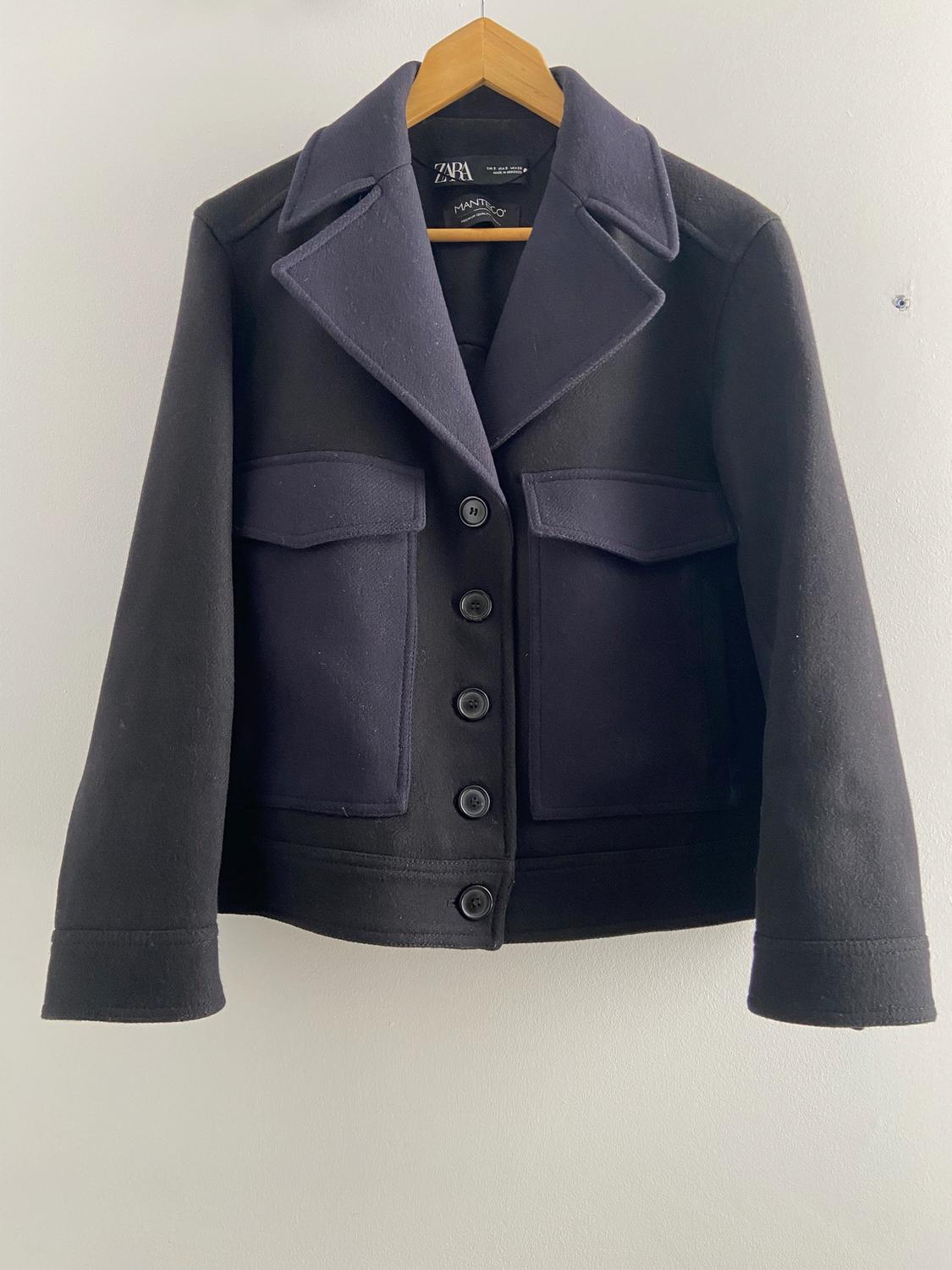 Black wool jacket with wide lapels and large buttons, hanging on a wooden hanger. Visible label: "ZARA".