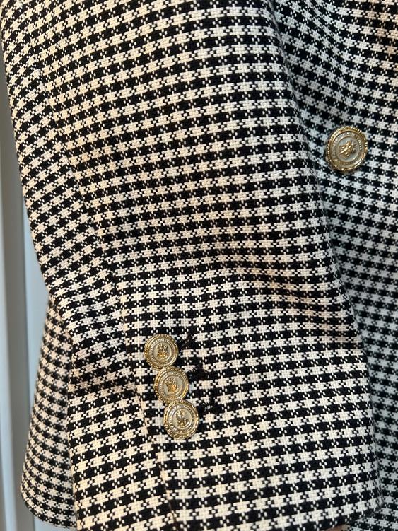 Close-up of a black and white checkered jacket, adorned with decorative gold buttons on the sleeve.