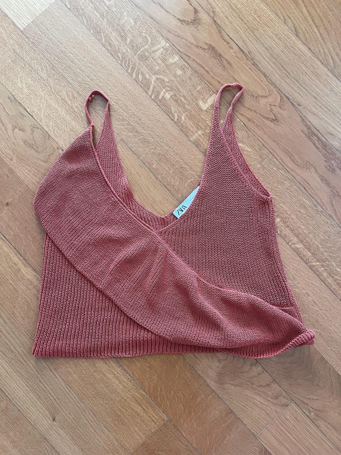 Terracotta knitted top with a V-neck and crossover detail, on a wooden floor. Label with the text ZARA.