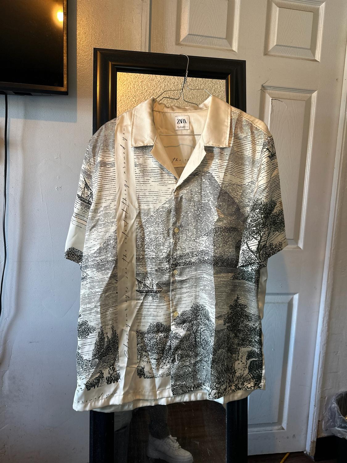 Landscape print shirt hanging on a mirror. Text: Close your eyes see the colorful things around you.