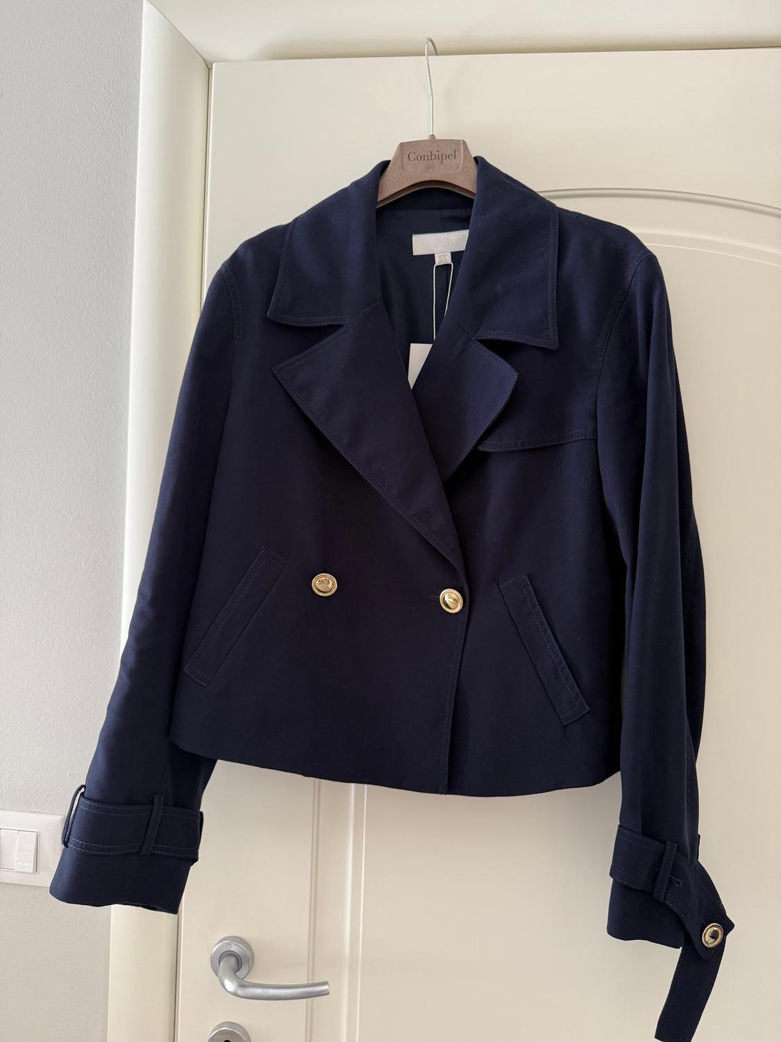 Navy blue jacket with gold buttons hanging on a wooden hanger with the brand "Conbipel", over a white door.