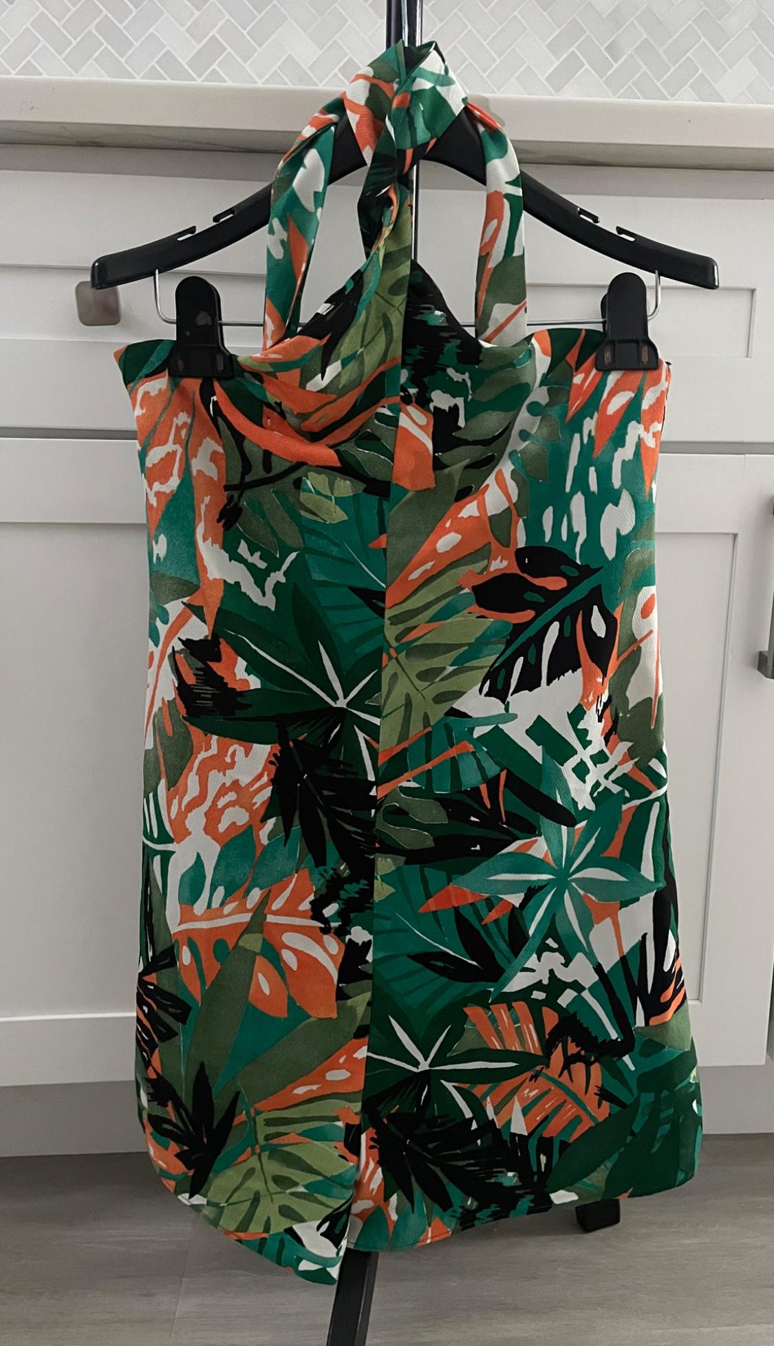 Front view of a dress with a tropical print in shades of green, orange and white, with a halter neck.