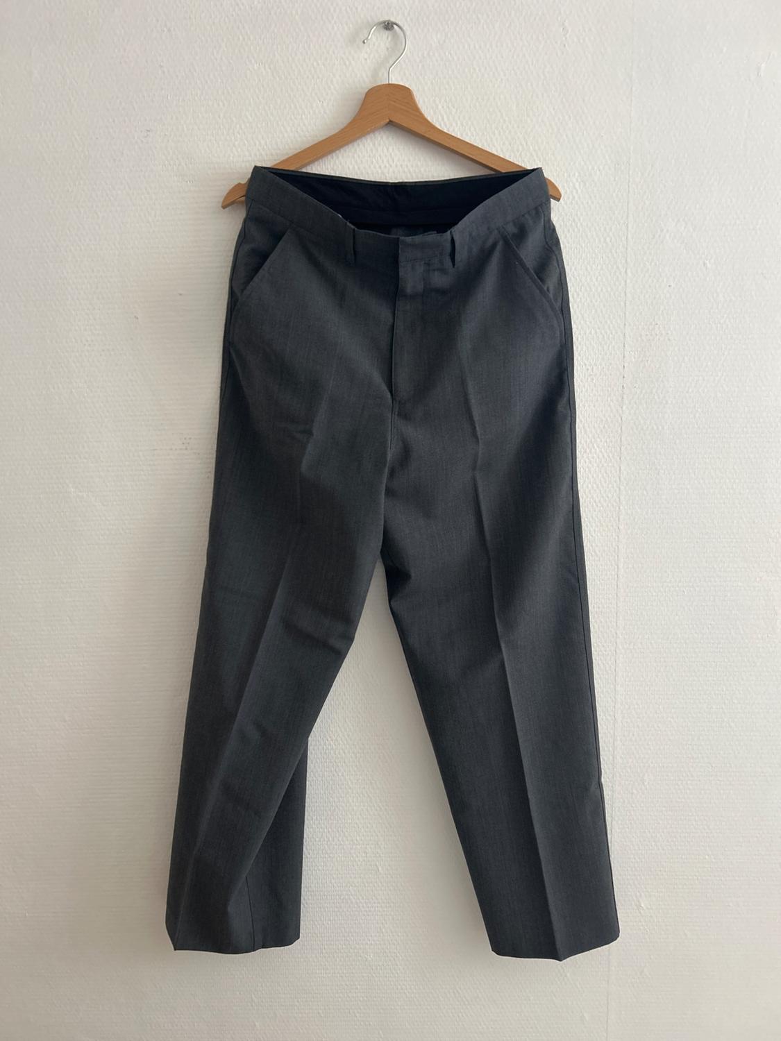 Grey dress trousers hanging on a wooden hanger against a white wall.