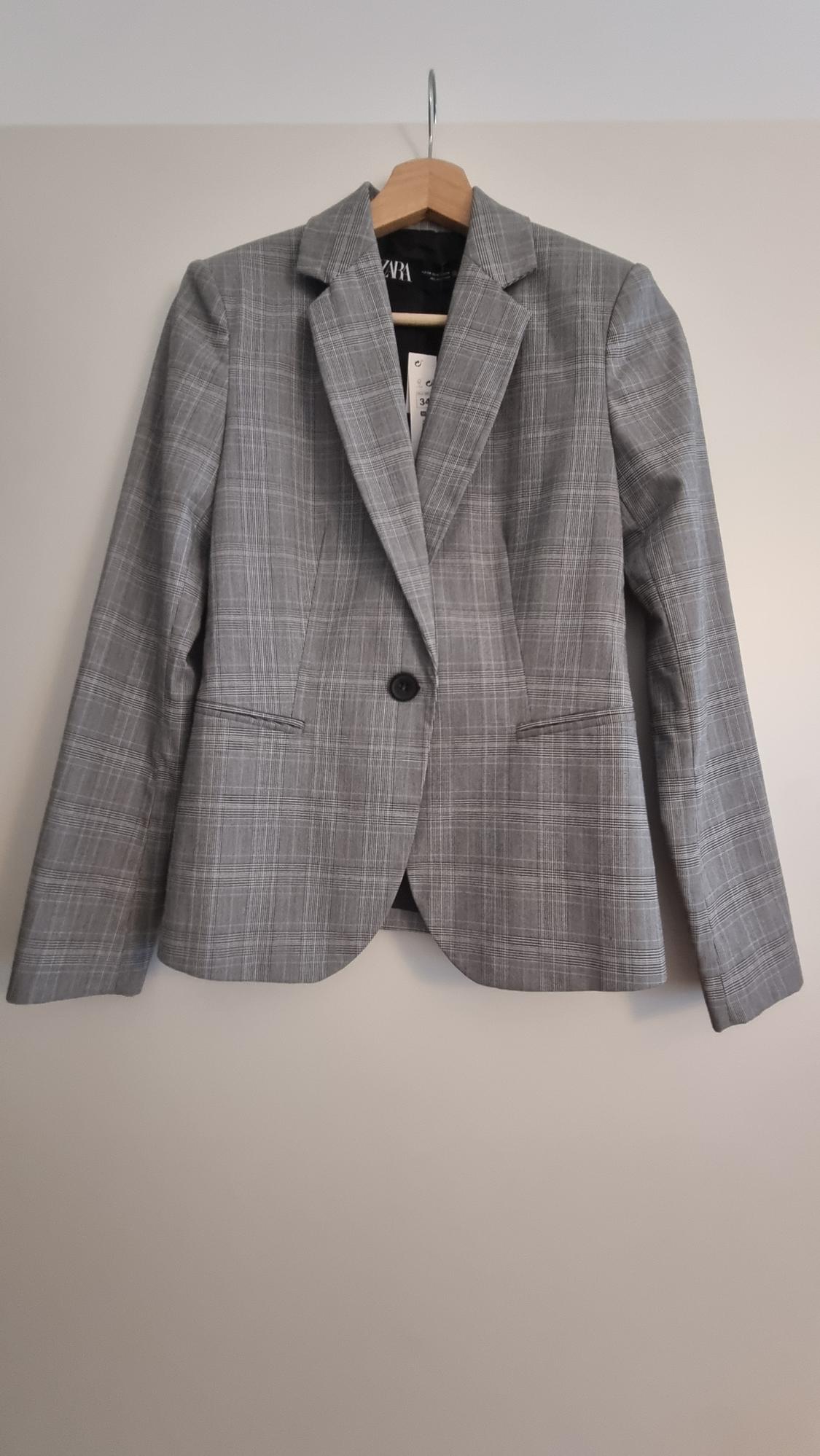 Grey checked jacket hanging on a wooden hanger. Visible label inside with the text "ZARA".