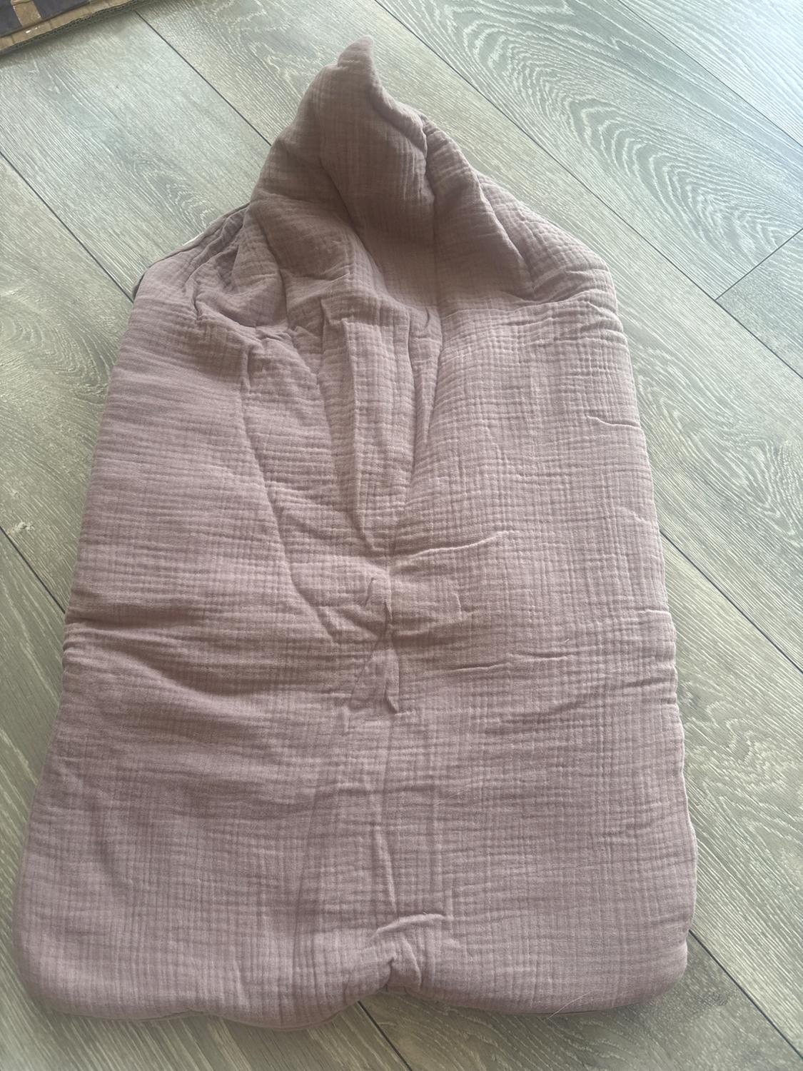 Baby sleeping bag with hood, in dusty pink crinkled fabric, on a light wood floor. Relaxed and cosy style.