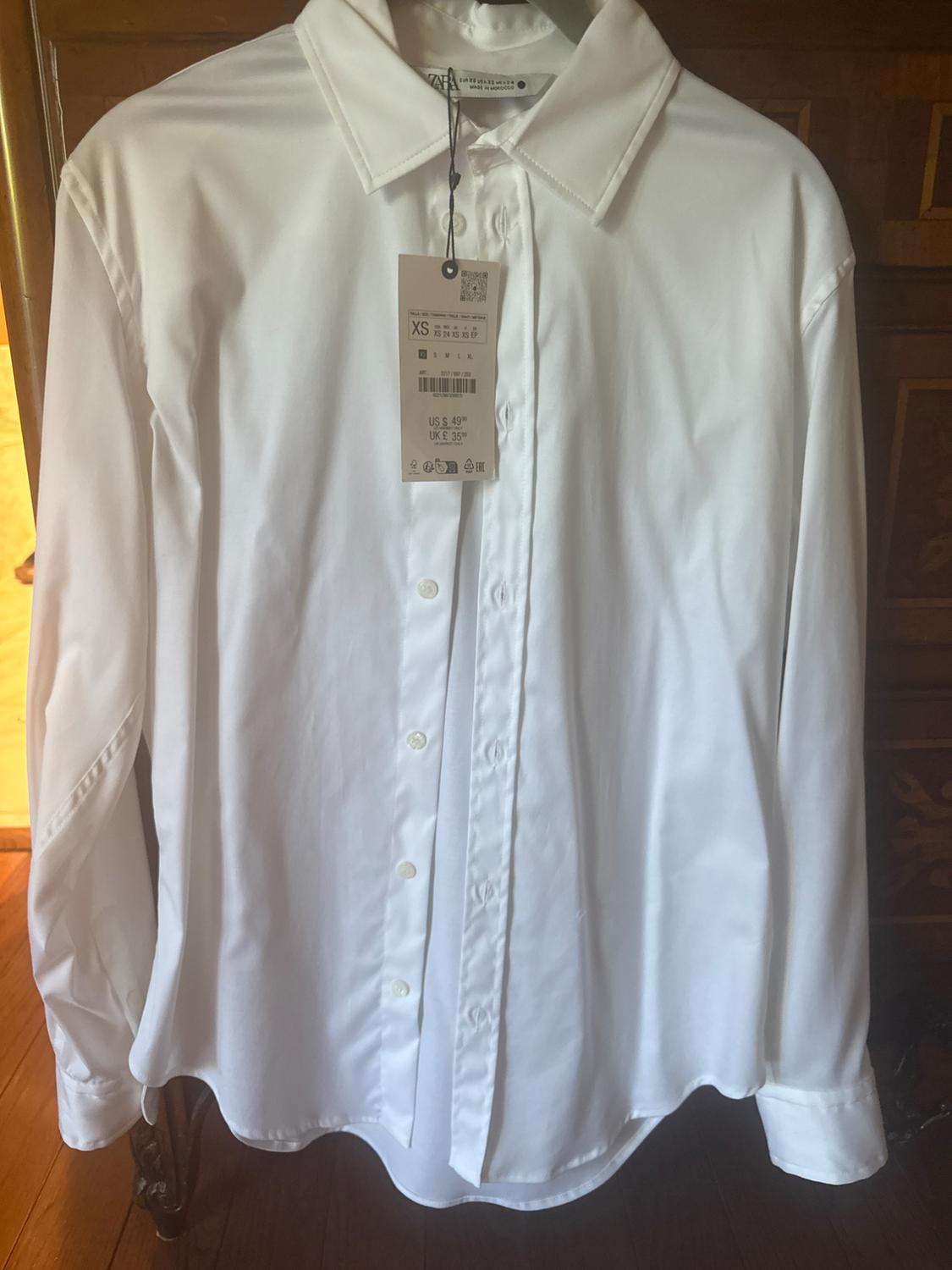 White long-sleeved shirt hanging on a hanger, with a visible tag indicating size XS and price US $49.99, UK £35.99.