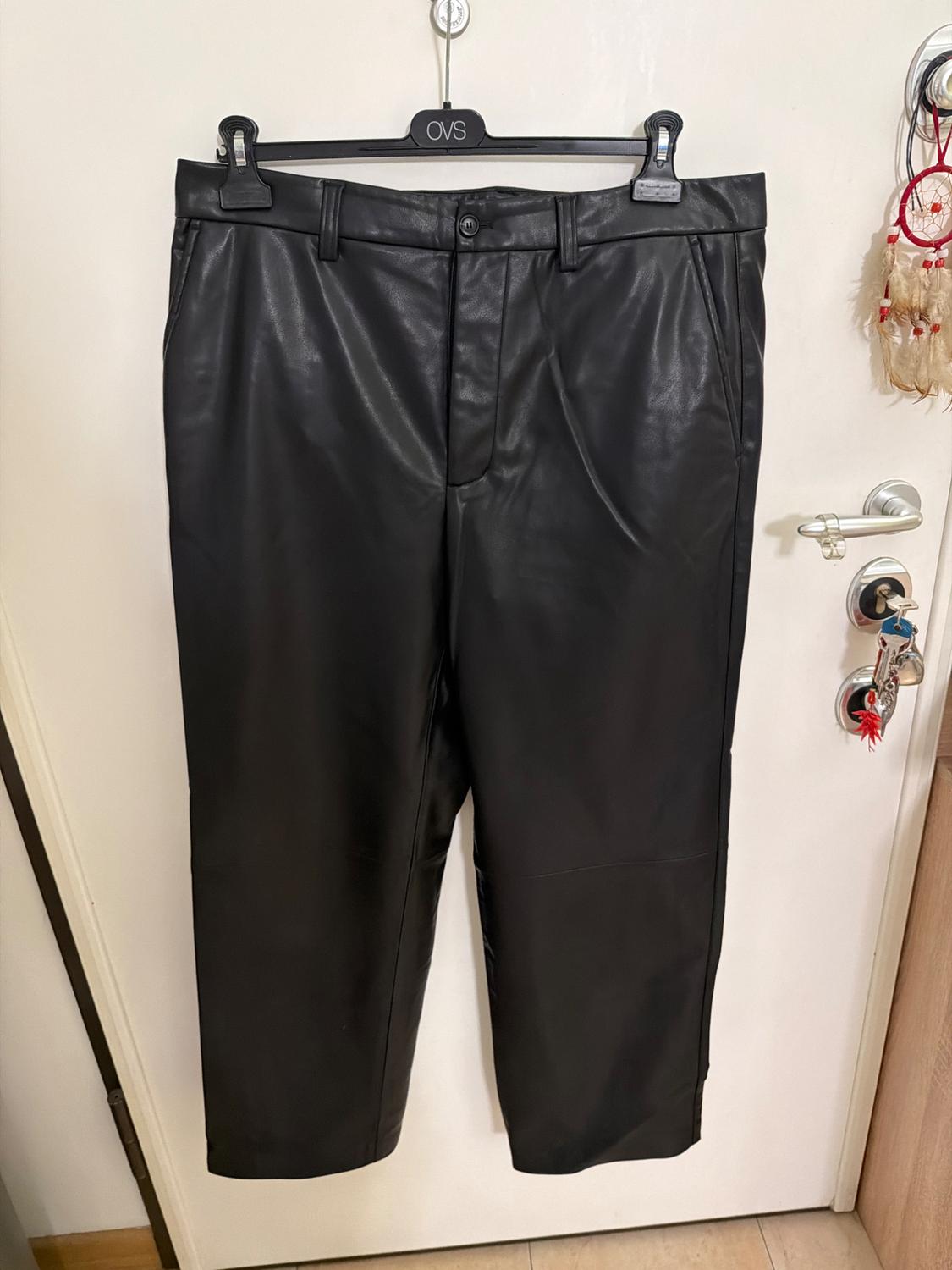 Black trousers hanging on a hanger with the text OVS on a white door with a handle, keys, and a dreamcatcher.