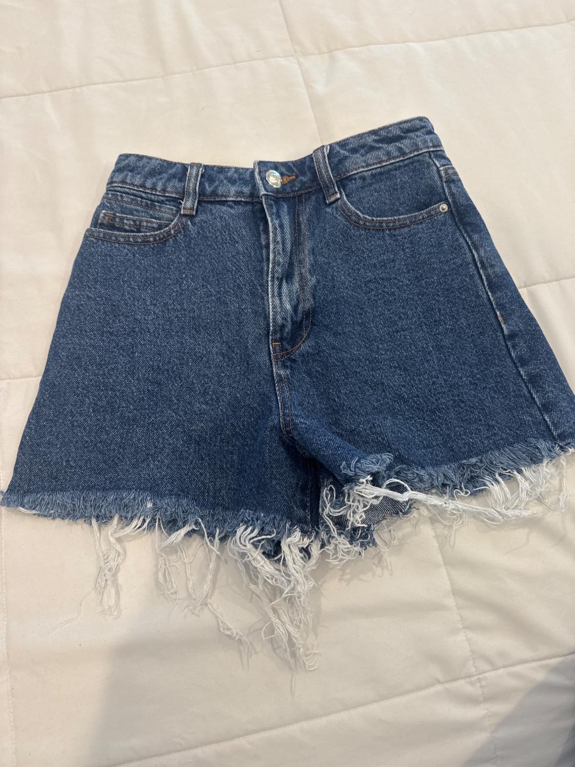 Blue denim shorts with a frayed hem on a quilted beige surface.